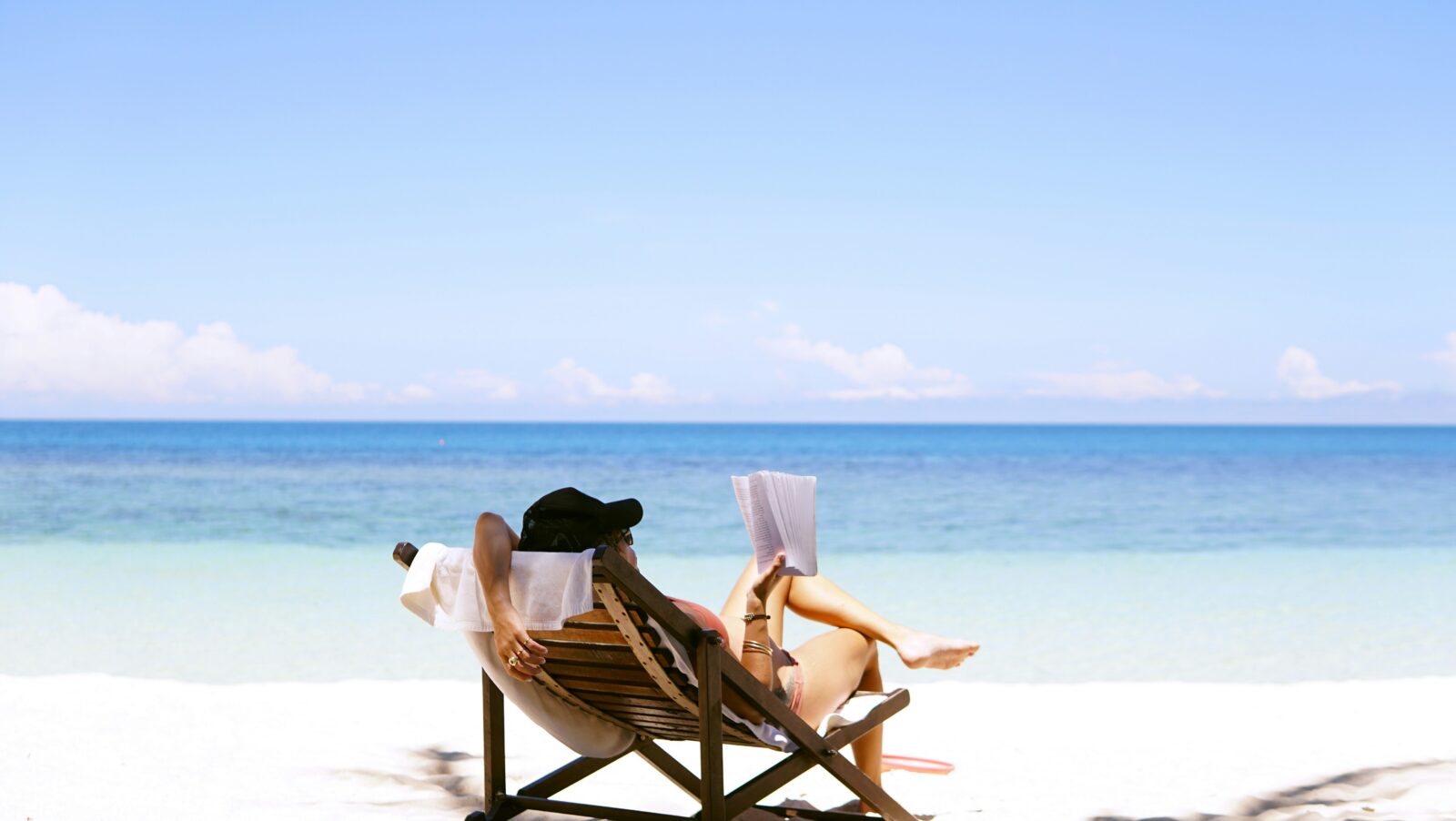 A person on a beach, sitting in a chair and reading a book.