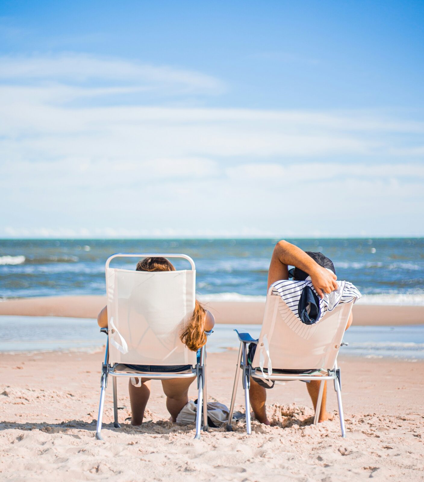 Two people sitting in lawn chairs on the beach looking at the ocean.